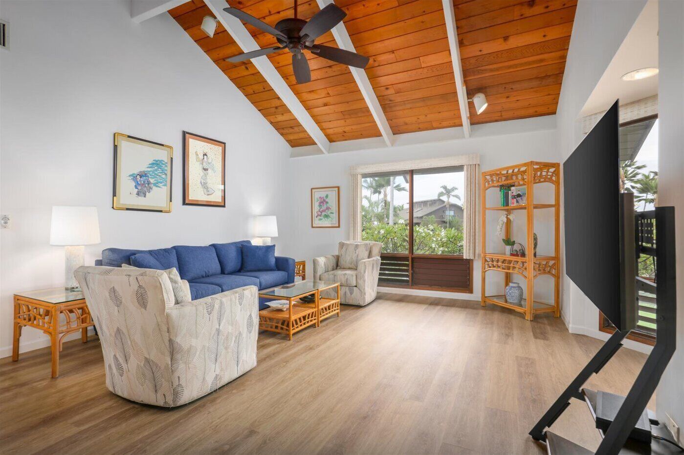 A spacious living room with a blue sofa, a patterned armchair, a glass coffee table, and a TV on a stand.