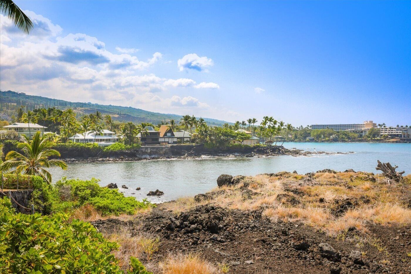 Une zone côtière avec des maisons situées près de l’eau, un ciel dégagé et un paysage vallonné en arrière-plan.