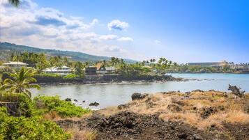A coastal area with houses near the water, a clear sky, and a hilly landscape in the background.
