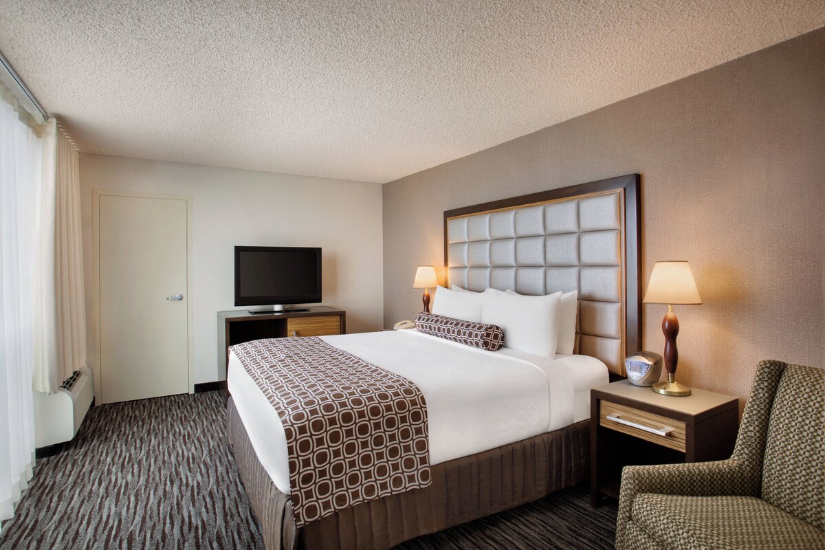 A hotel room with a large bed, two bedside lamps, a flat-screen TV, a chair, and a dresser.
