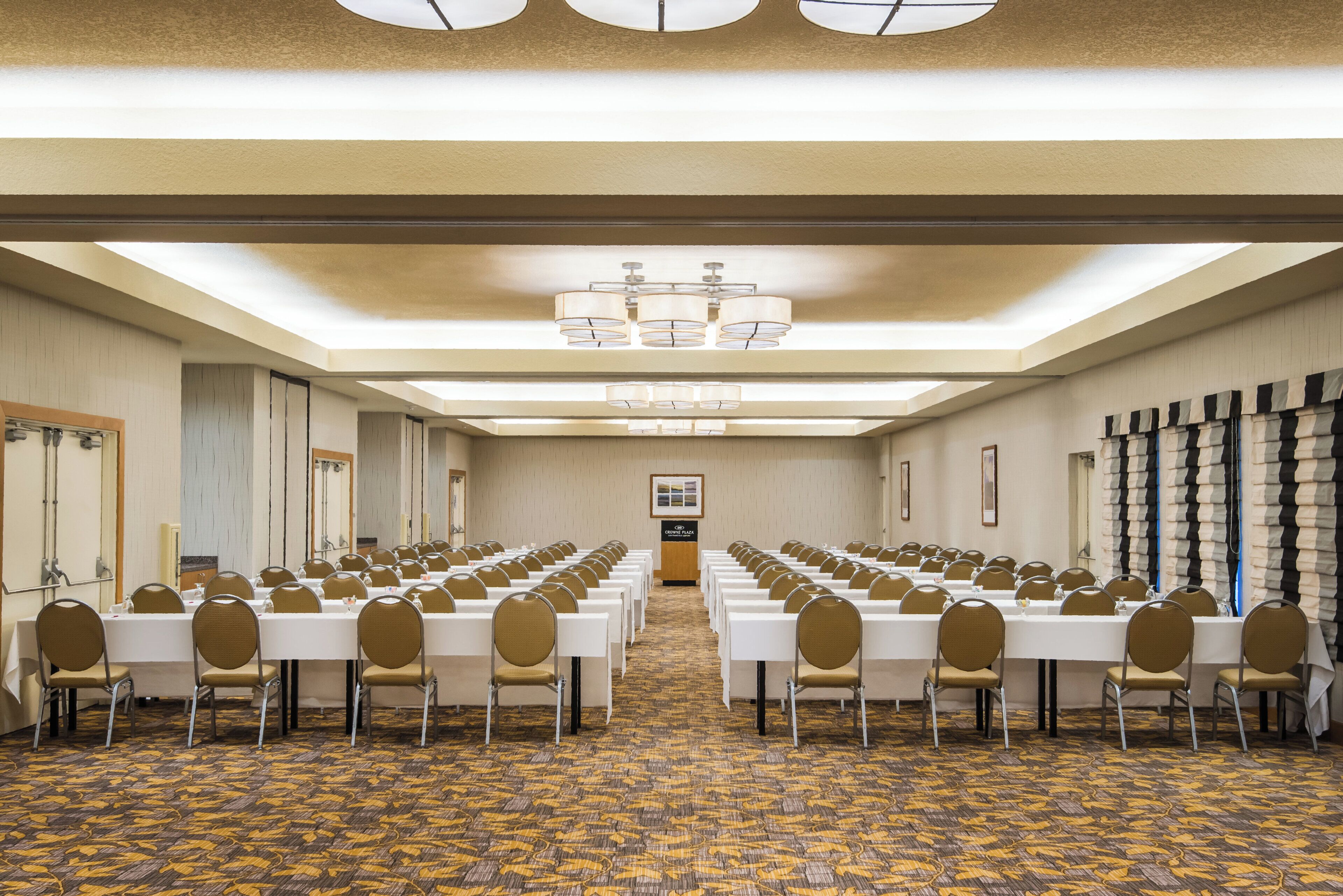 Un salón de conferencias con filas de mesas y sillas, una alfombra estampada y un candelabro.