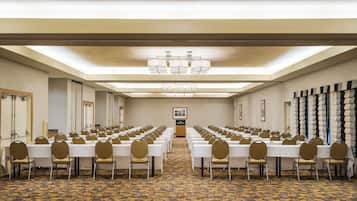 Un salón de conferencias con filas de mesas y sillas, una alfombra estampada y un candelabro.