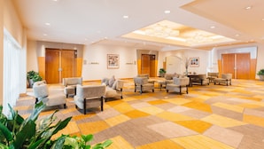 Un hall d’hôtel avec un tapis à carreaux, plusieurs espaces aménagés avec des sièges et des portes en bois portant les inscriptions « SALLE DE BAINS 1 » et « SALLE DE BAINS 2 ».