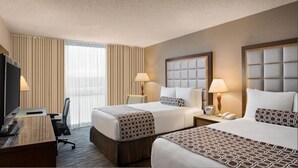 A hotel room with two beds, a desk, a chair, a TV, and a window with curtains.