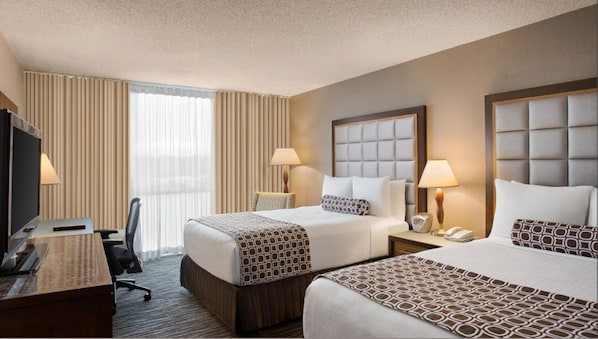A hotel room with two beds, a desk, a chair, a TV, and a window with curtains.