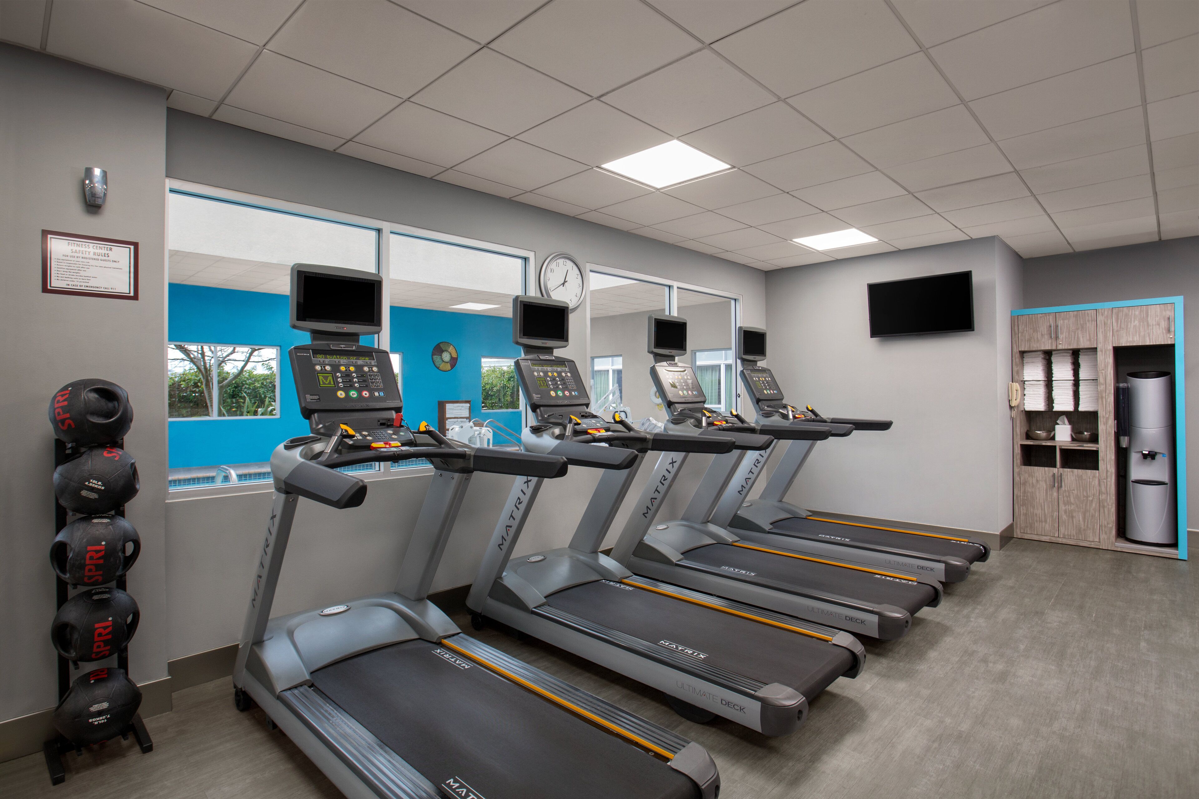 Une salle de sport équipée de tapis de course, de ballons d’exercice et d’une horloge au mur.