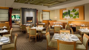 Une salle à manger d’hôtel avec plusieurs tables dressées pour les clients, une cheminée et un grand tableau abstrait accroché au mur.