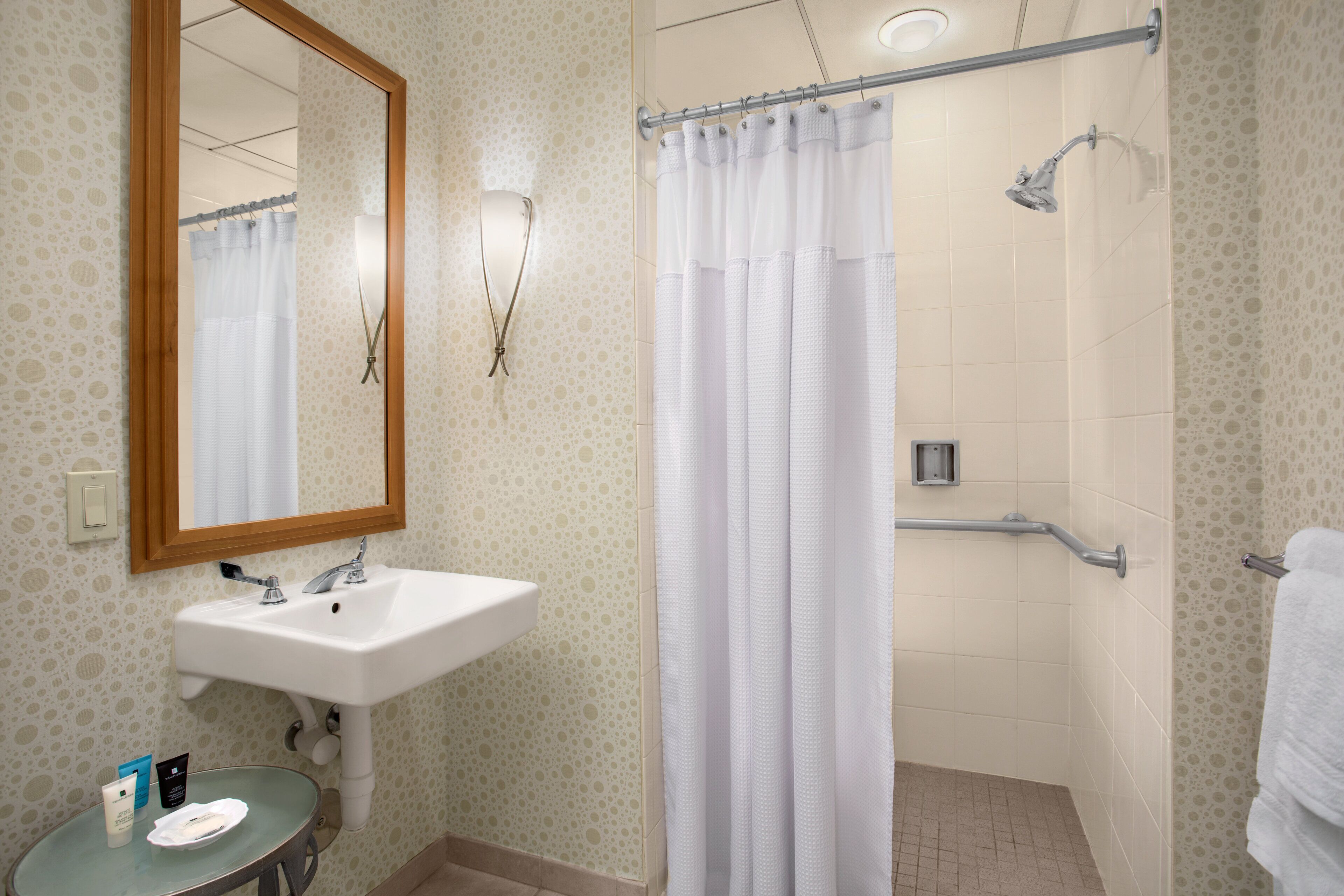 A bathroom with a sink, mirror, shower, and towel rack.