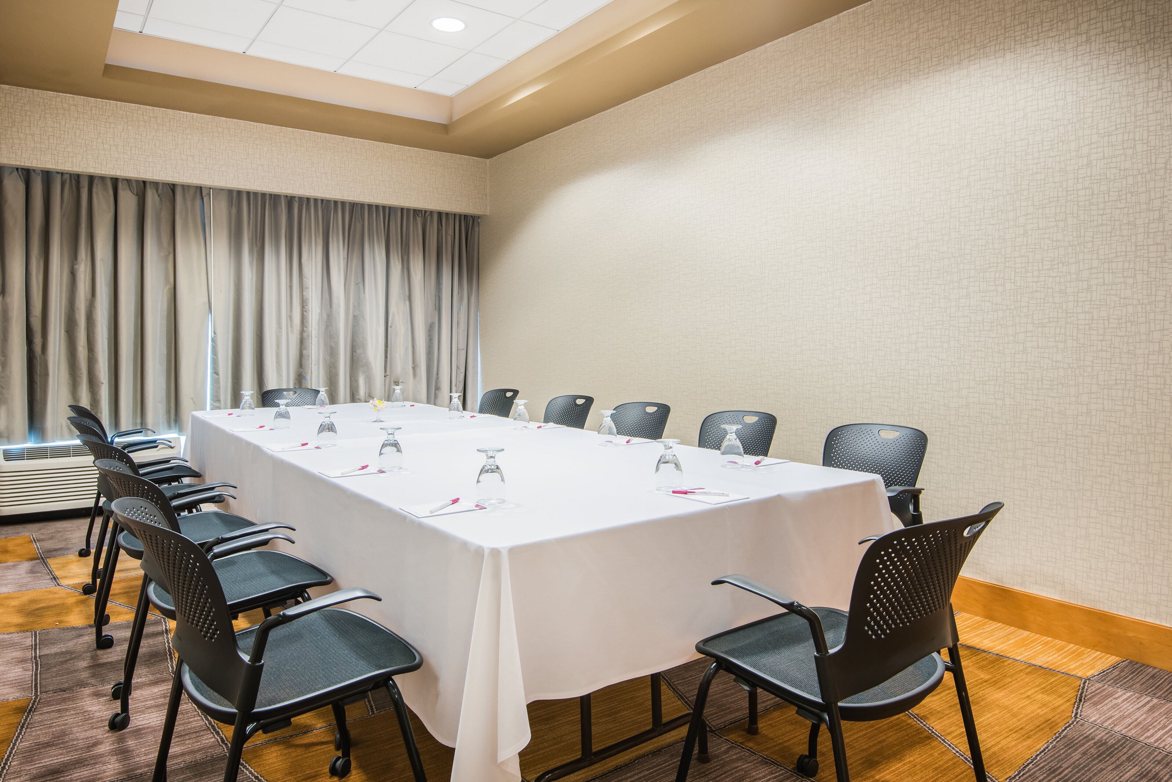 A conference room with a long table, chairs, and a window with curtains.