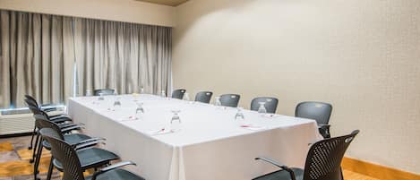 A conference room with a long table, chairs, and a window with curtains.