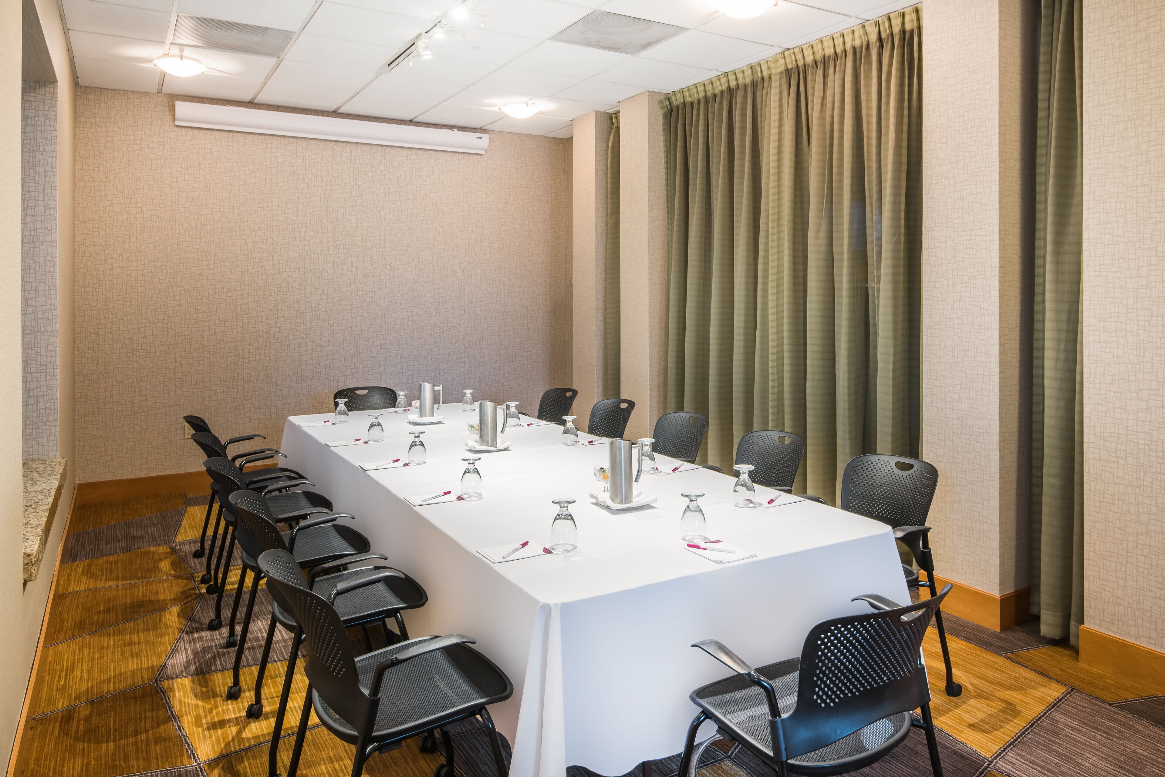 Uma sala de conferências com uma mesa comprida, cadeiras pretas e toalha de mesa branca.