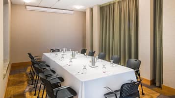 Uma sala de conferências com uma mesa comprida, cadeiras pretas e toalha de mesa branca.