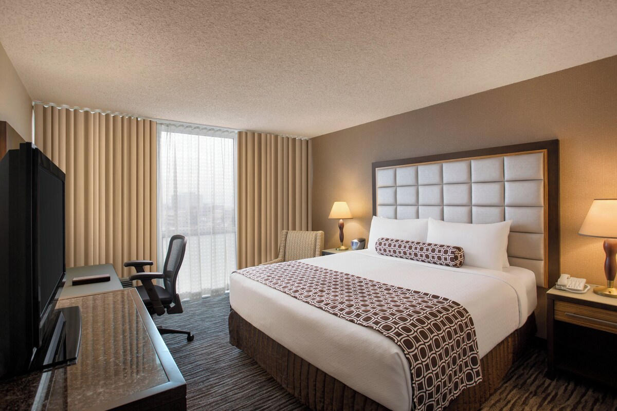 A hotel room with a large bed, a desk with a chair, a television, and a window with curtains.