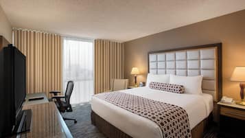 A hotel room with a large bed, a desk with a chair, a television, and a window with curtains.