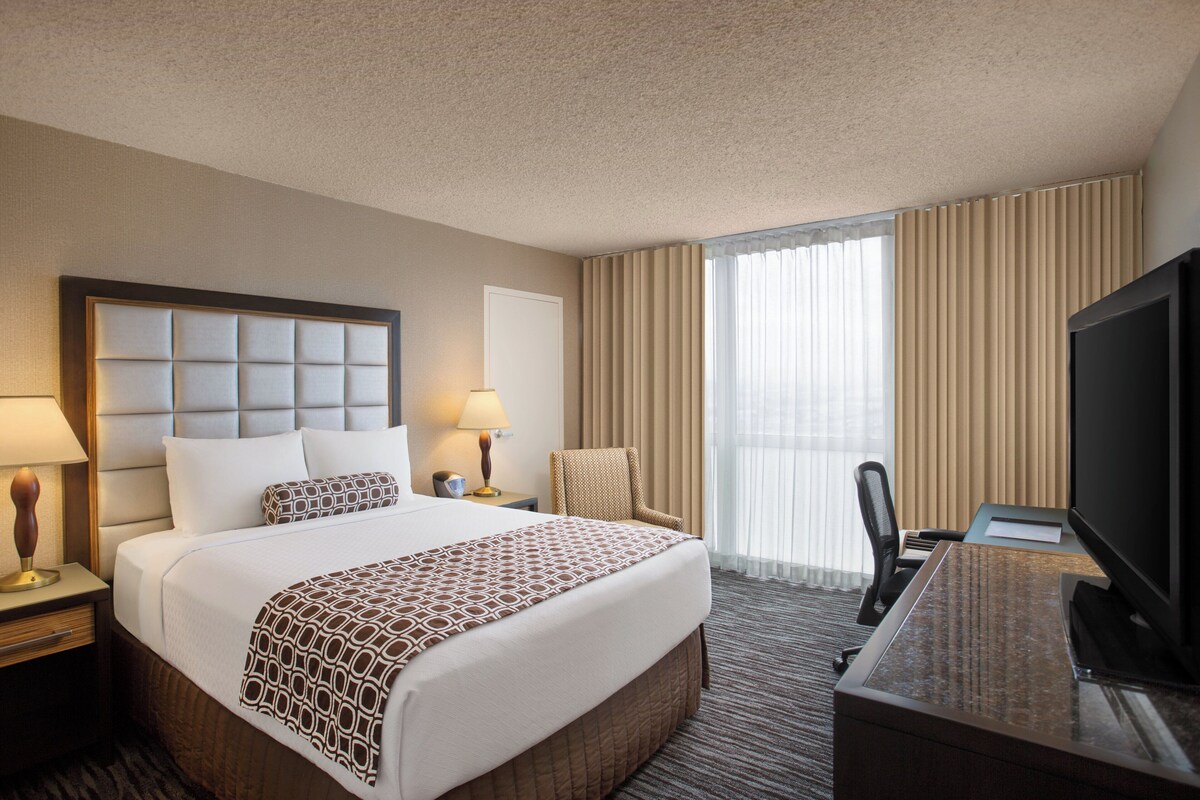 A hotel room with a large bed, a desk with a television, a chair, and a window with curtains.