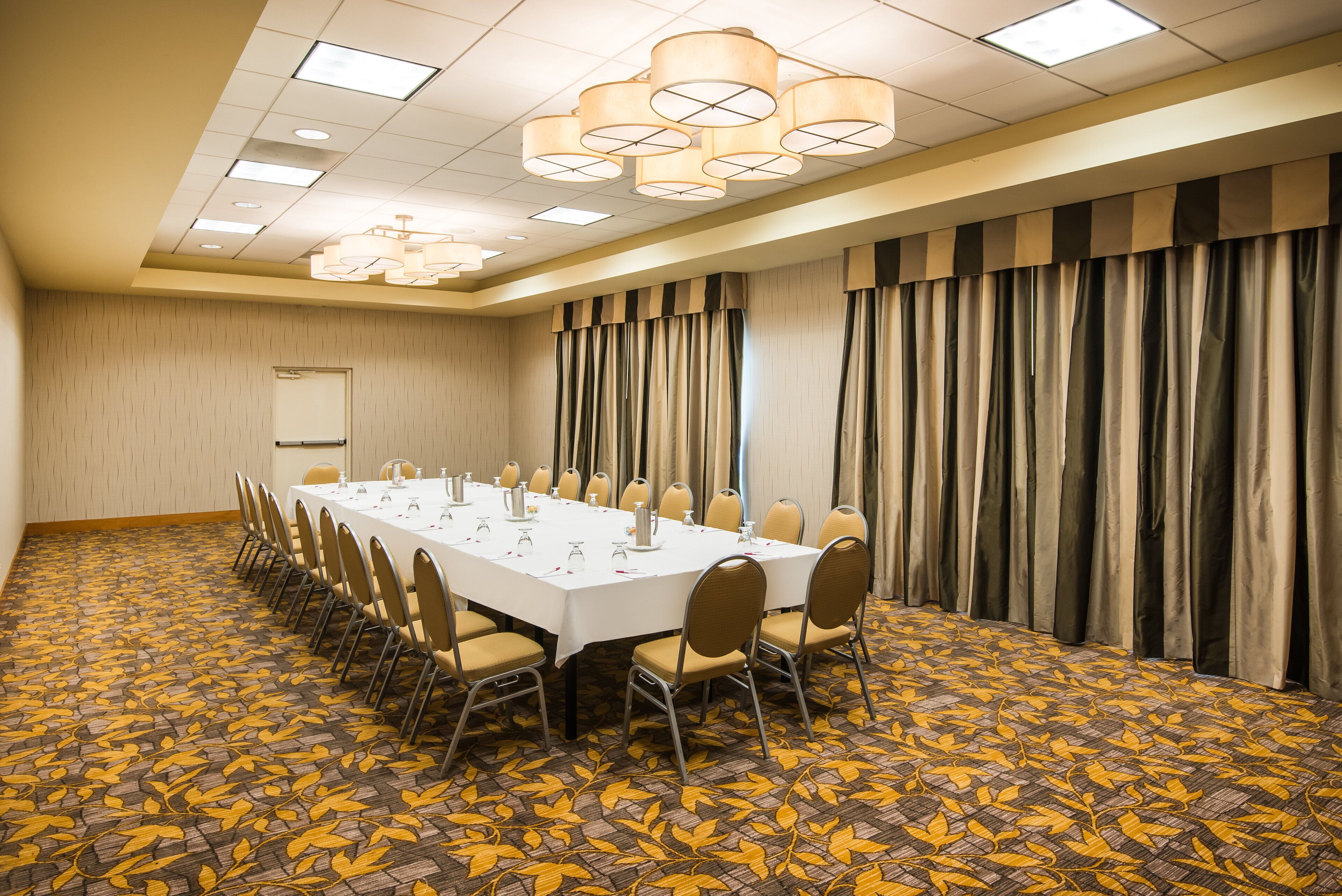 Un salón de conferencias con una larga mesa, sillas y una alfombra estampada.