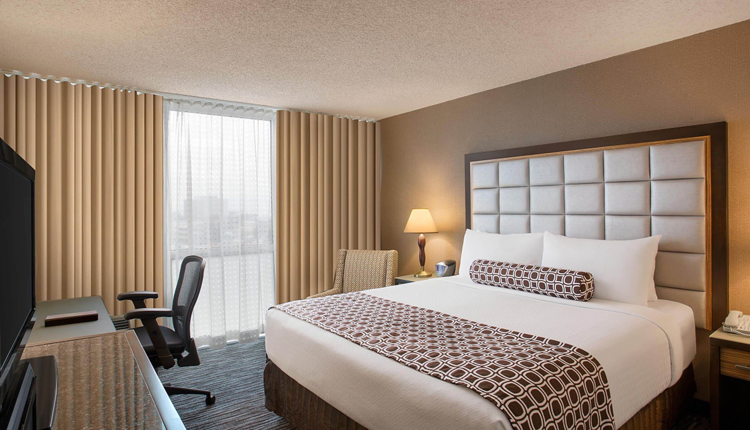A hotel room with a large bed, a desk, a chair, a lamp, and a telephone.