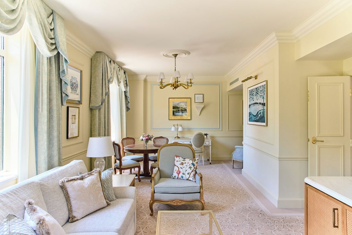 A room with a sofa, armchair, dining table, chandelier, and framed artwork.