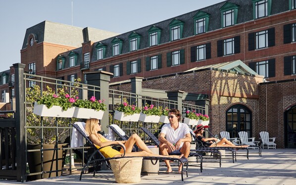 A rooftop patio with lounge chairs and planters, overlooking a brick building with green window frames.