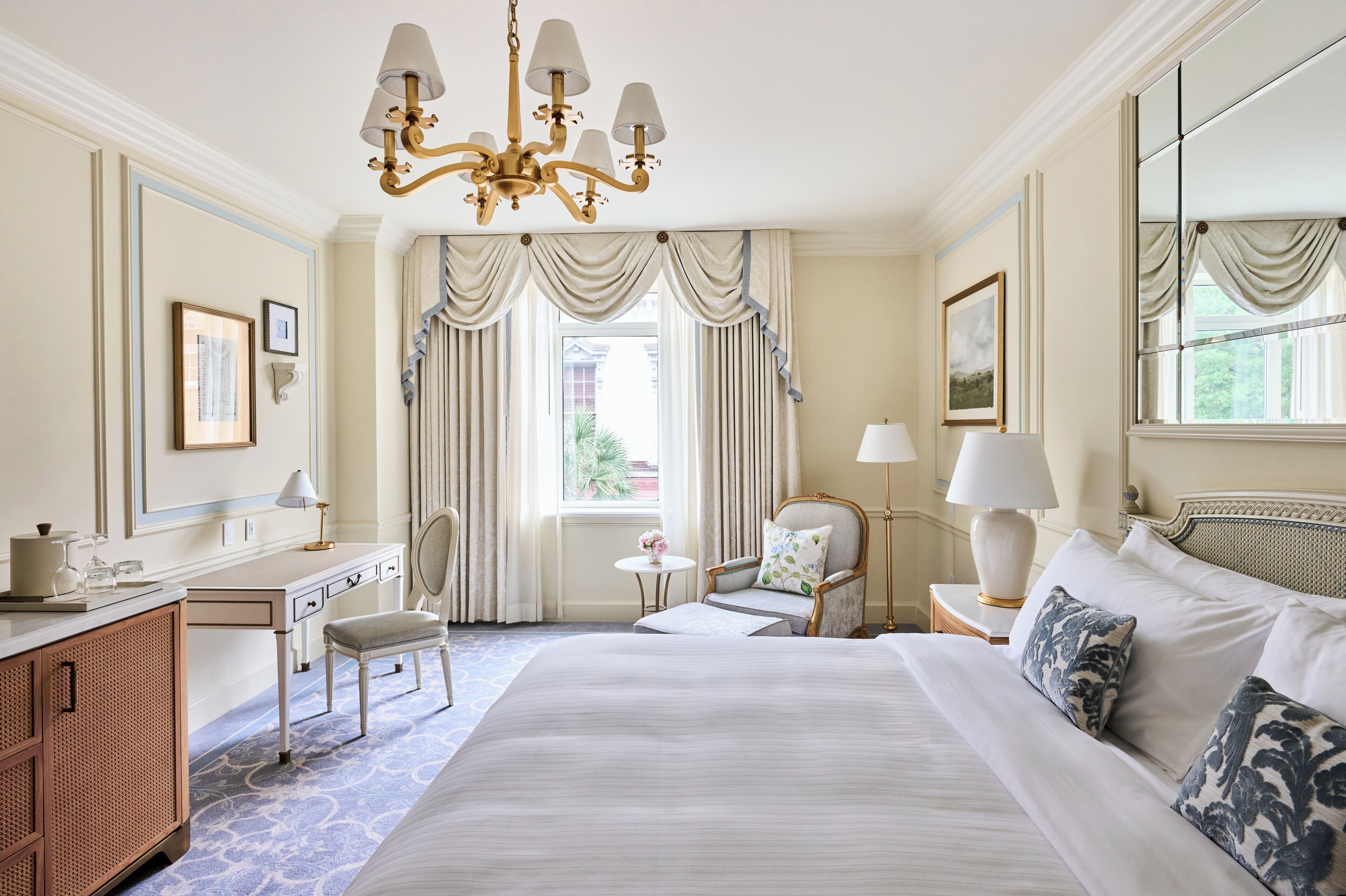 Une chambre d’hôtel avec un grand lit, un bureau, une chaise, une petite table et un lustre.
