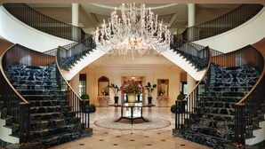 A grand lobby with a marble staircase, a large chandelier, and a central table with flowers. - The Charleston Place (Charleston)