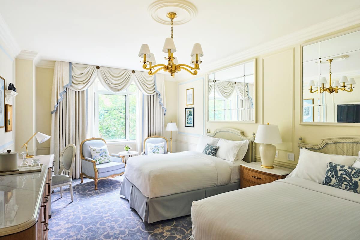 A hotel room with two beds, a sitting area, a desk, and a large mirror.