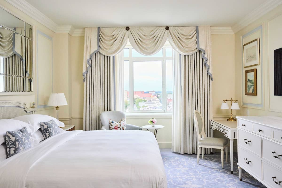 A hotel room with a large bed, a desk, a chair, a dresser, and a window with curtains.