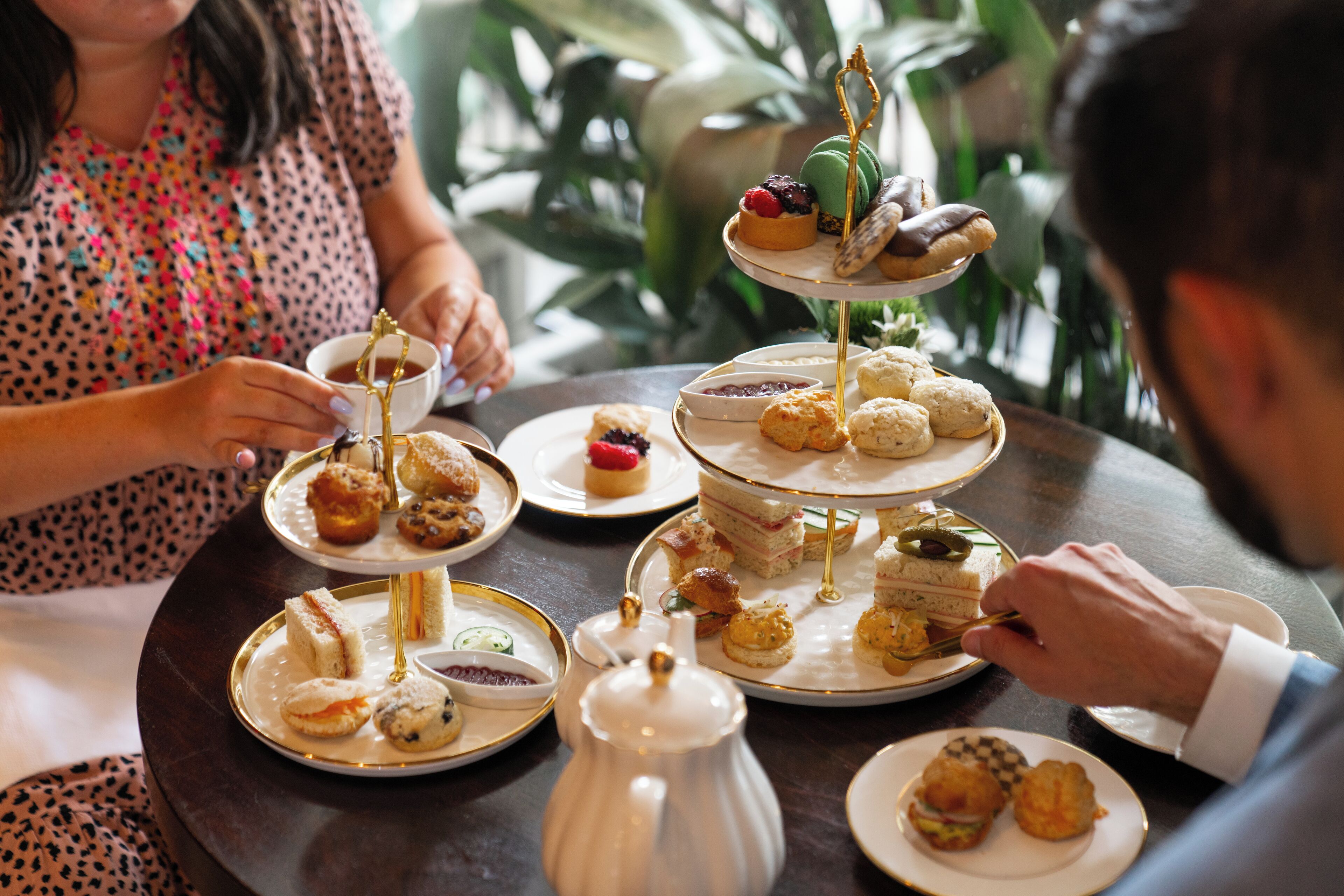 Una mesa redonda con múltiples platos de postres escalonados, una tetera y una taza.
