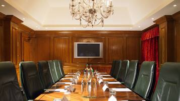 A conference room with a long table, green leather chairs, a chandelier, and a television on the wall.