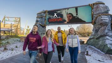 A group of people walking on a wooden pathway with a large outdoor screen displaying 'The Bear Grylls Adventure' text.