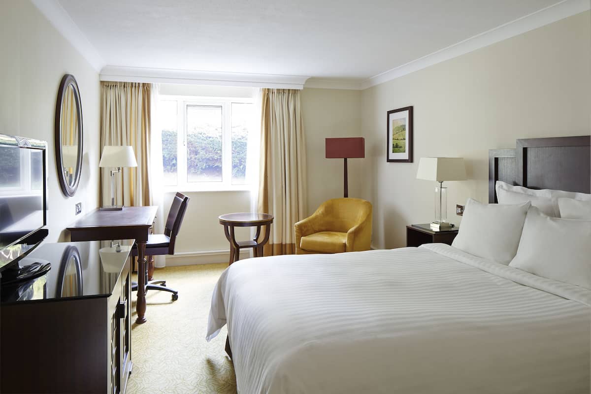Ein Hotelzimmer mit einem großen Bett, einem Schreibtisch mit Stuhl, einem kleinen Tisch, einer Couch und einem Fernseher.