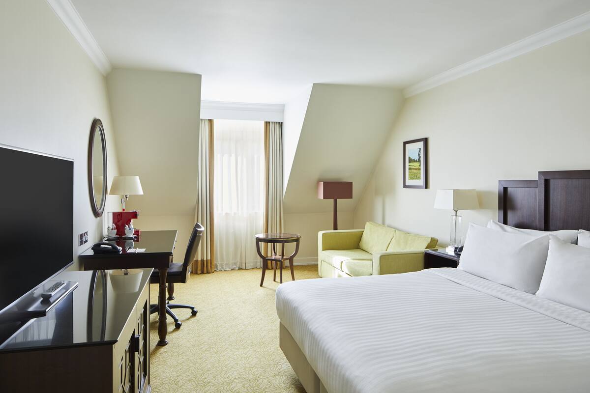 Ein Hotelzimmer mit einem Bett, einem Schreibtisch mit Computer, einem Sessel, einem kleinen Tisch und einer Lampe.