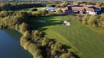 Vista aérea de un campo de golf con un club house, un estanque y follaje circundante.