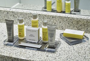 Presentación de productos A.C.C.A. KAPPA que incluye jabón líquido, champú, acondicionador, gel de ducha, loción corporal y una caja de loción corporal sobre una encimera de granito.