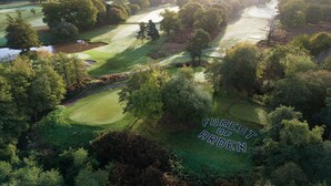Luftaufnahme eines Golfplatzes mit Teich, umgeben von dichtem Baumbestand und einem Fluss.