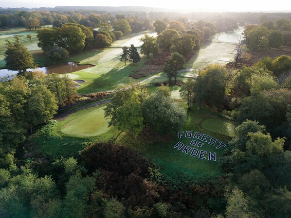 An aerial view of a golf course with a pond, surrounded by dense trees and a river. - Forest of Arden Hotel & Country Club (Solihull)