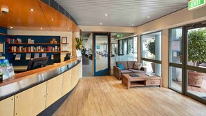 A reception area with a wooden reception desk, a sofa, and a coffee table. There are bookshelves with books and a sign indicating a guest library. - Broadwater Resort Como (Como)