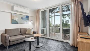 A modern living room with a sofa, a small round table, a flat-screen TV mounted on the wall, and a sliding glass door leading to an outdoor area.