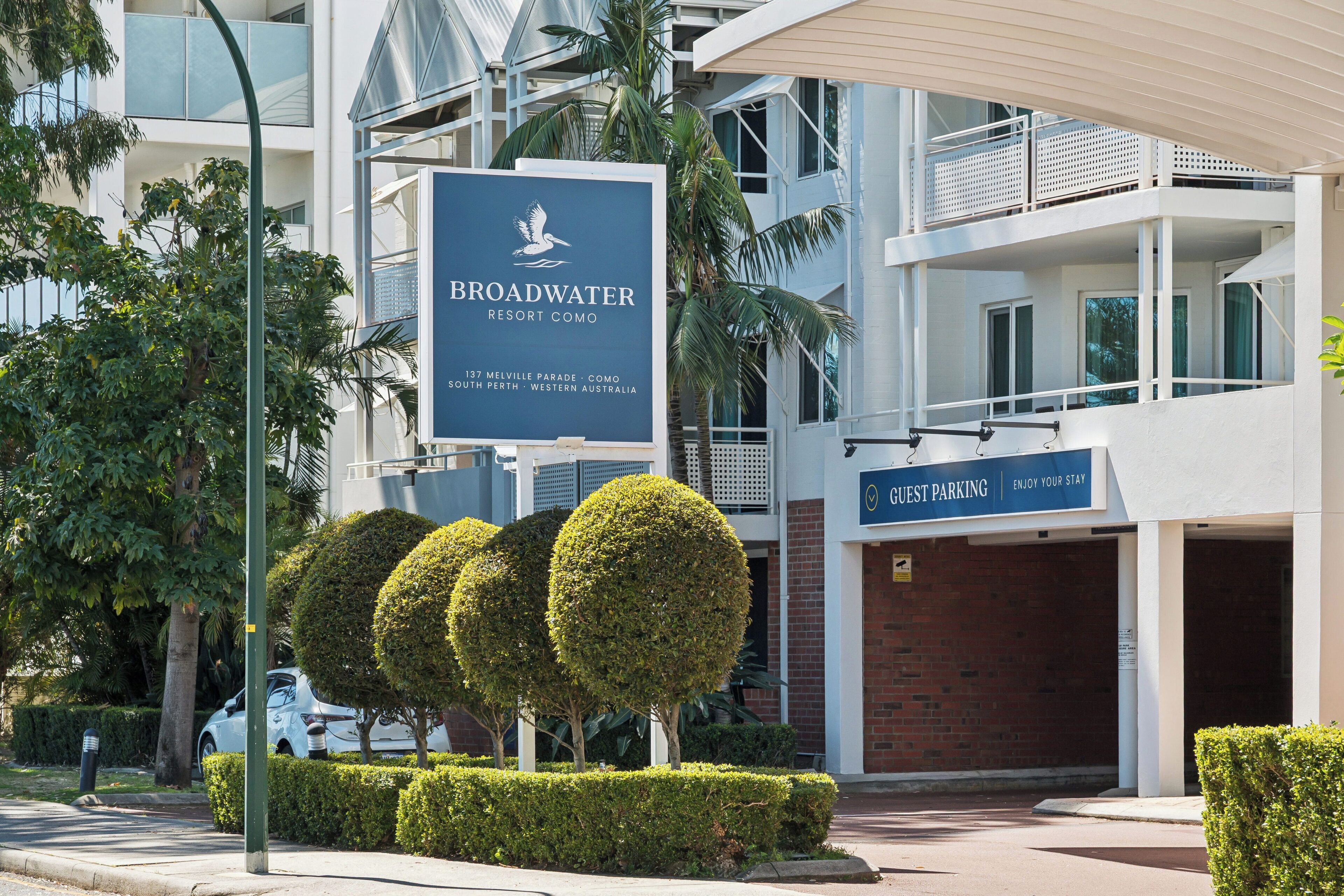 A sign for Broadwater Resort Como with a view of the building's architecture and landscaping.
