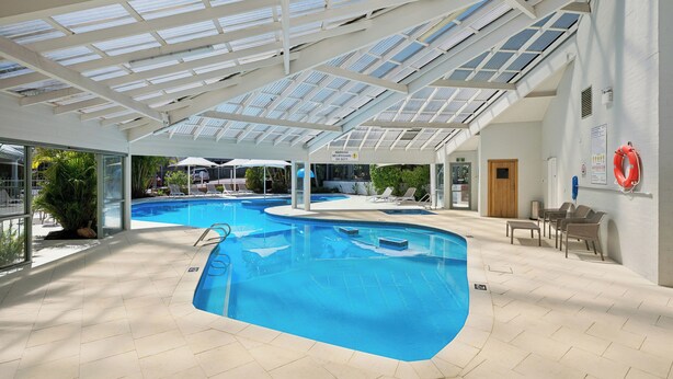 An indoor swimming pool with a glass ceiling, lounge chairs, and a lifebuoy on the wall. - Broadwater Resort Como (Como)
