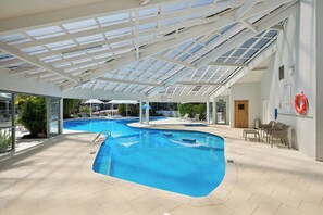 An indoor swimming pool with a glass ceiling, lounge chairs, and a lifebuoy on the wall.