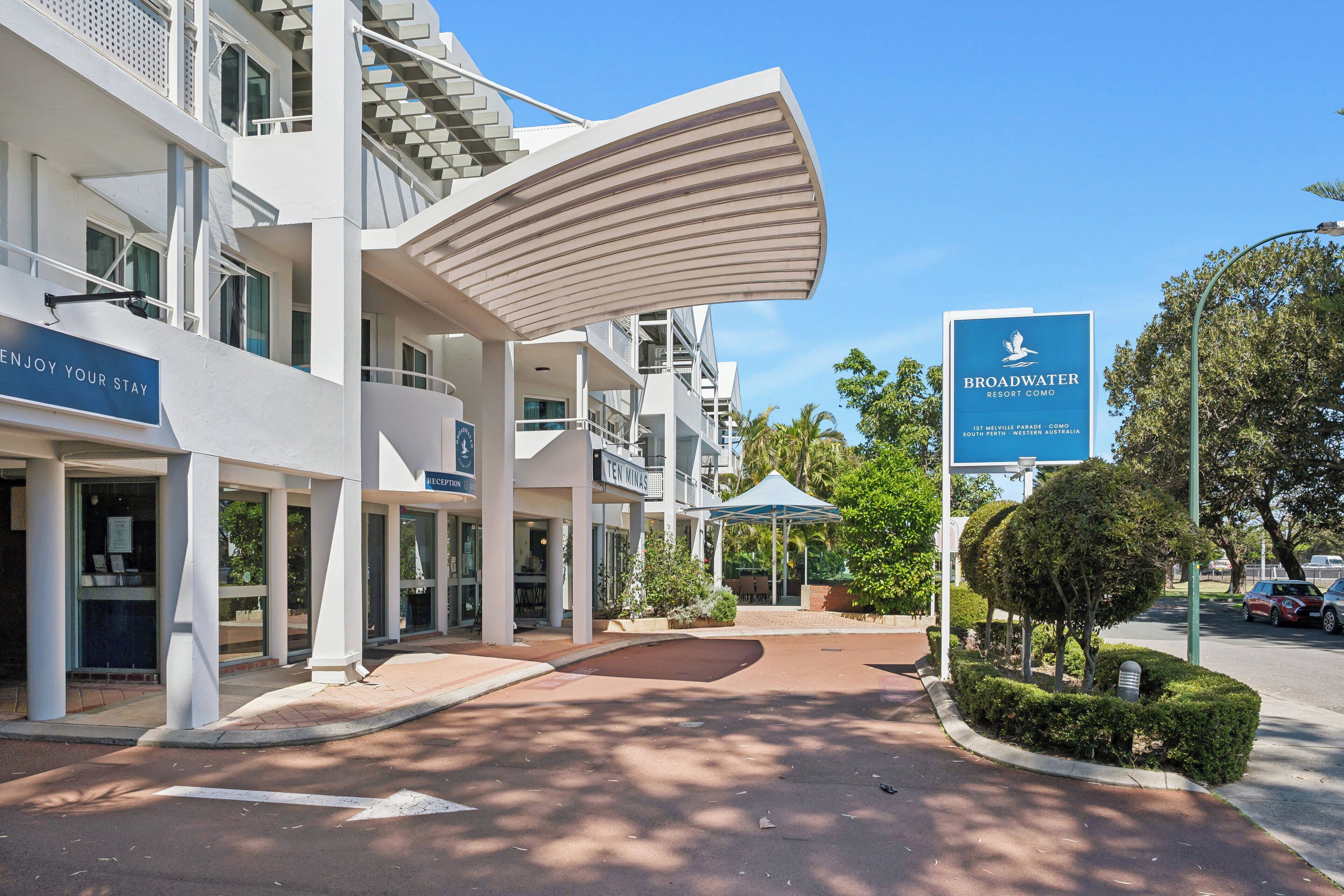 Un edificio moderno con una zona de recepción, un cartel que dice 'Broadwater Resort Como', y un cielo despejado.