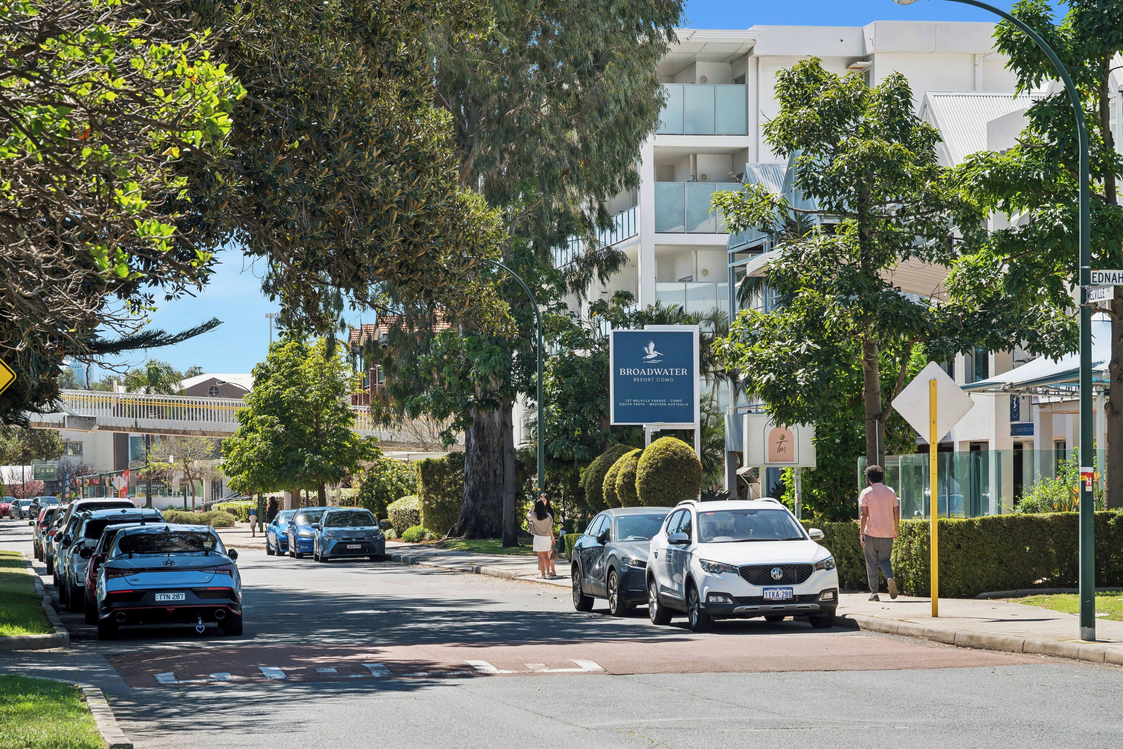 A street view with parked cars, a sign for Broadwater Resort Como, and a building with balconies.