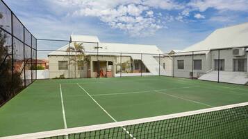 Ein Tennisplatz mit Netz, umzäunt und mit angrenzenden Gebäuden.