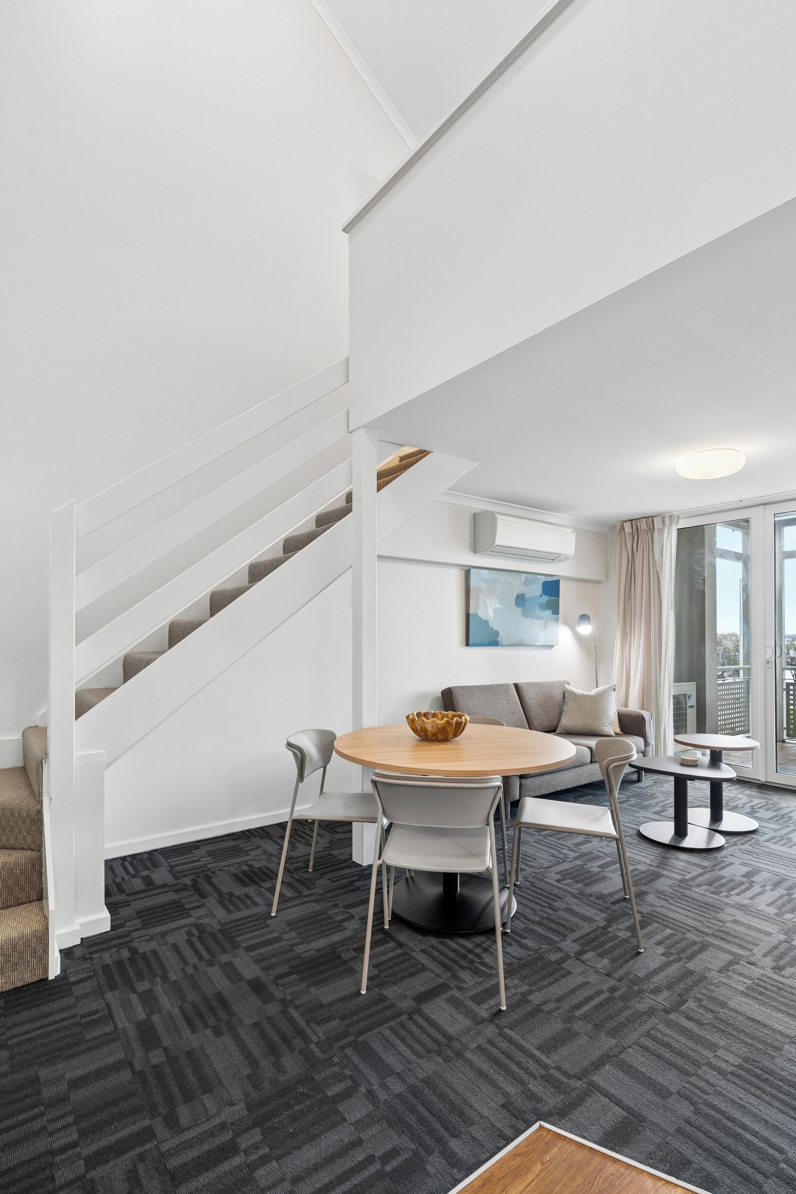 A modern living room with a staircase, a dining area with a round table, and a sofa.