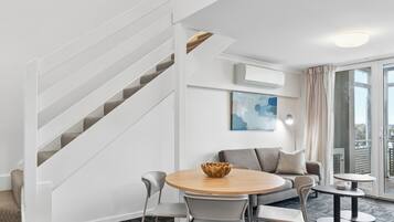 A modern living room with a staircase, a dining area with a round table, and a sofa.