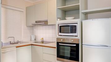 Una cucina compatta con mobili bianchi, un forno a microonde integrato, un forno in acciaio inox e un frigorifero bianco.
