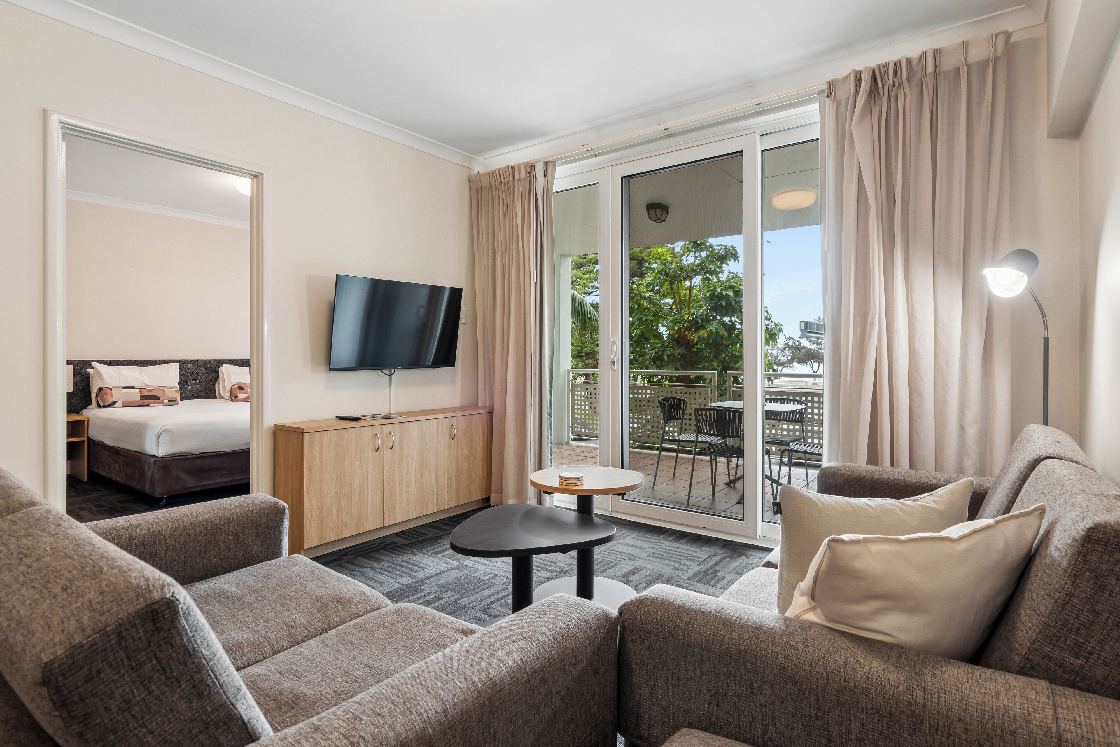 Habitación de hotel con sofá, una mesita, televisor y balcón con vistas a zonas verdes.