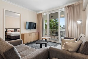 Habitación de hotel con sofá, una mesita, televisor y balcón con vistas a zonas verdes.