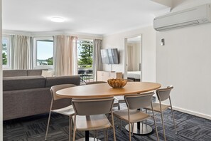 Una habitación de hotel moderna con sofá, mesa de comedor, sillas, televisor y aire acondicionado.